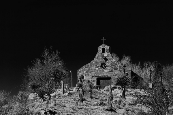 A black and white photo of a church with trees in the foreground.