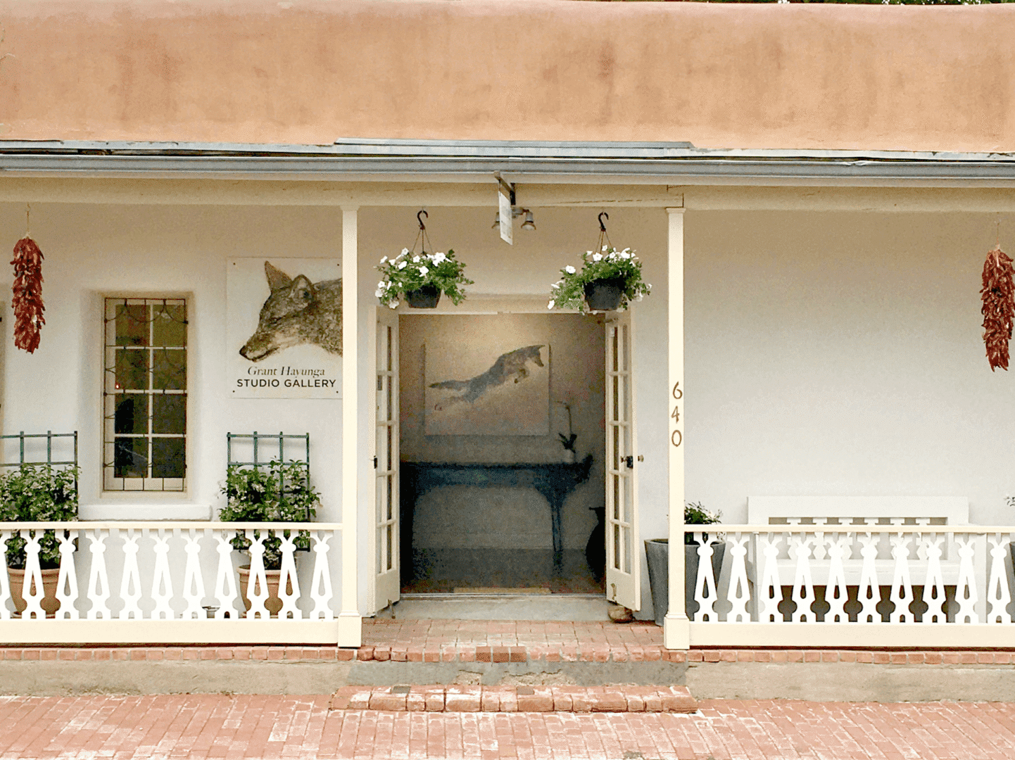 A white porch with potted plants and horse pictures.